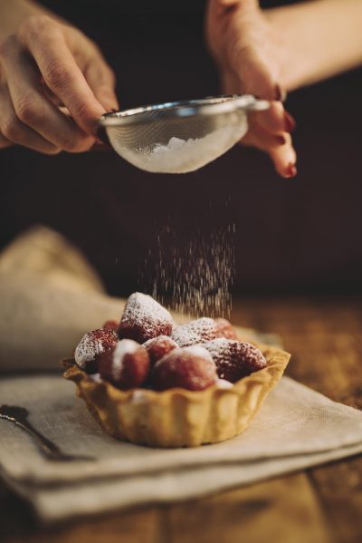 close-up-woman-dusting-sugar-powder-strawberry-tart (Copy)